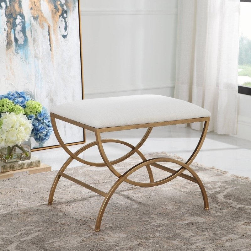 Brushed brass arch-base accent stool with an off-white upholstered top