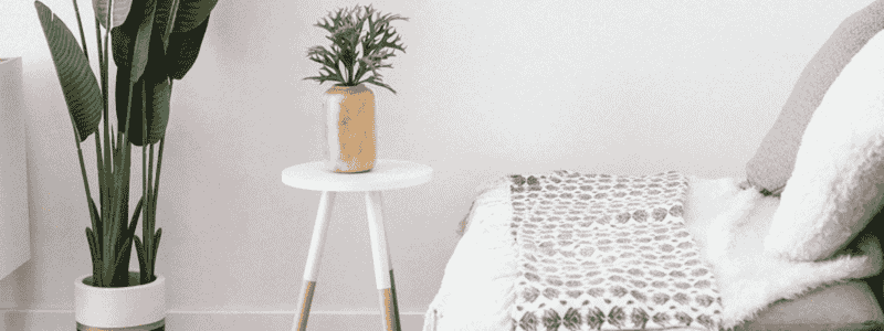 Cozy corner with a chair, small table, and potted plant against a white wall.