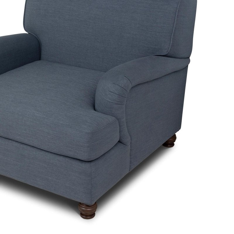 Close-up of the Kenwood heathered navy blue chair upholstery, loose seat cushion, rounded arm and turned wood foot