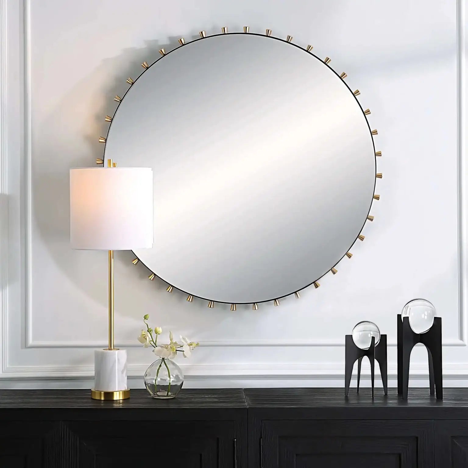 Round wall mirror with decorative frame on a white wall above a dark wooden console table.